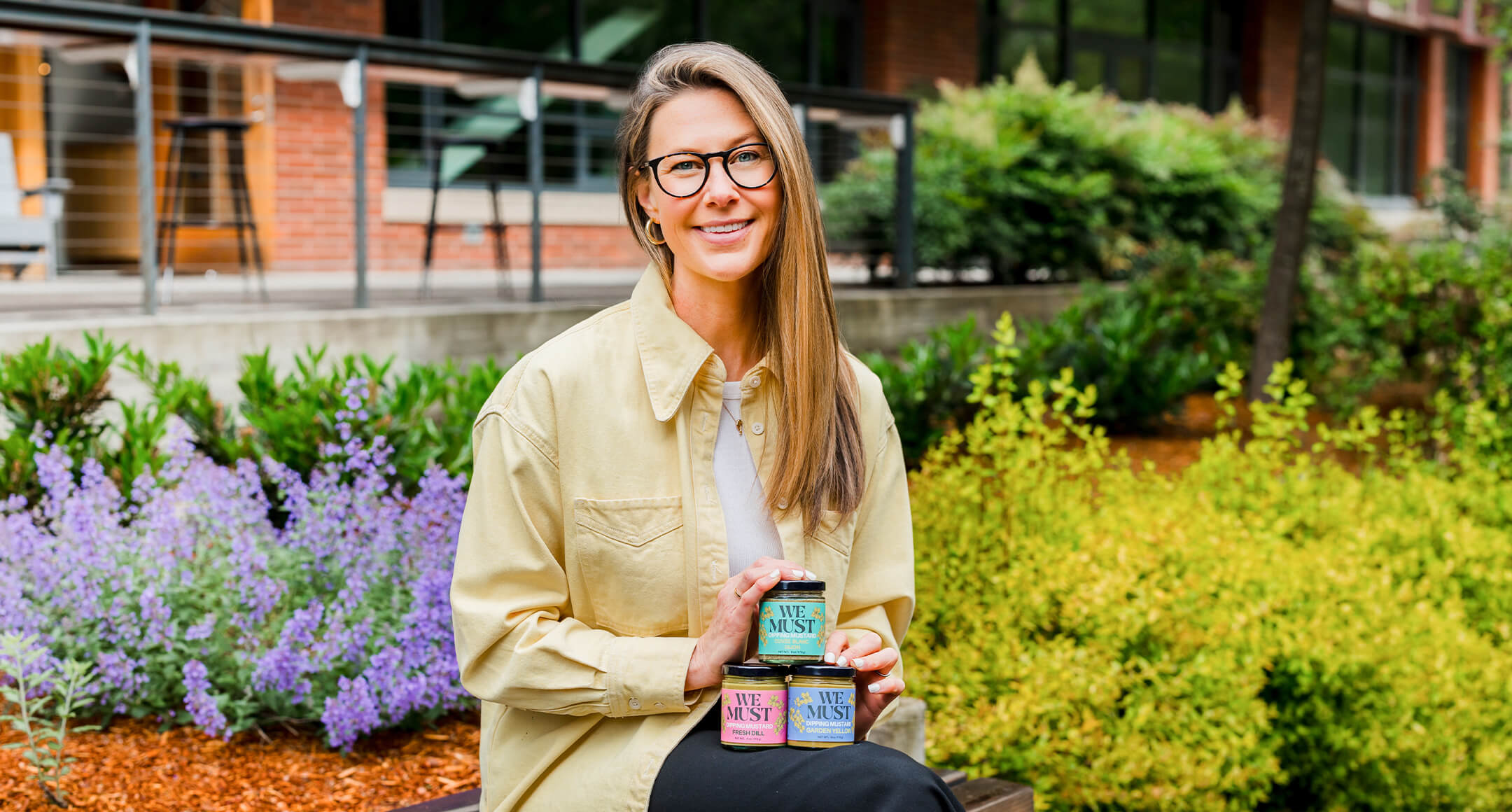 We Must Mustard founder Courtney Yones holding three jars of her mustard.
