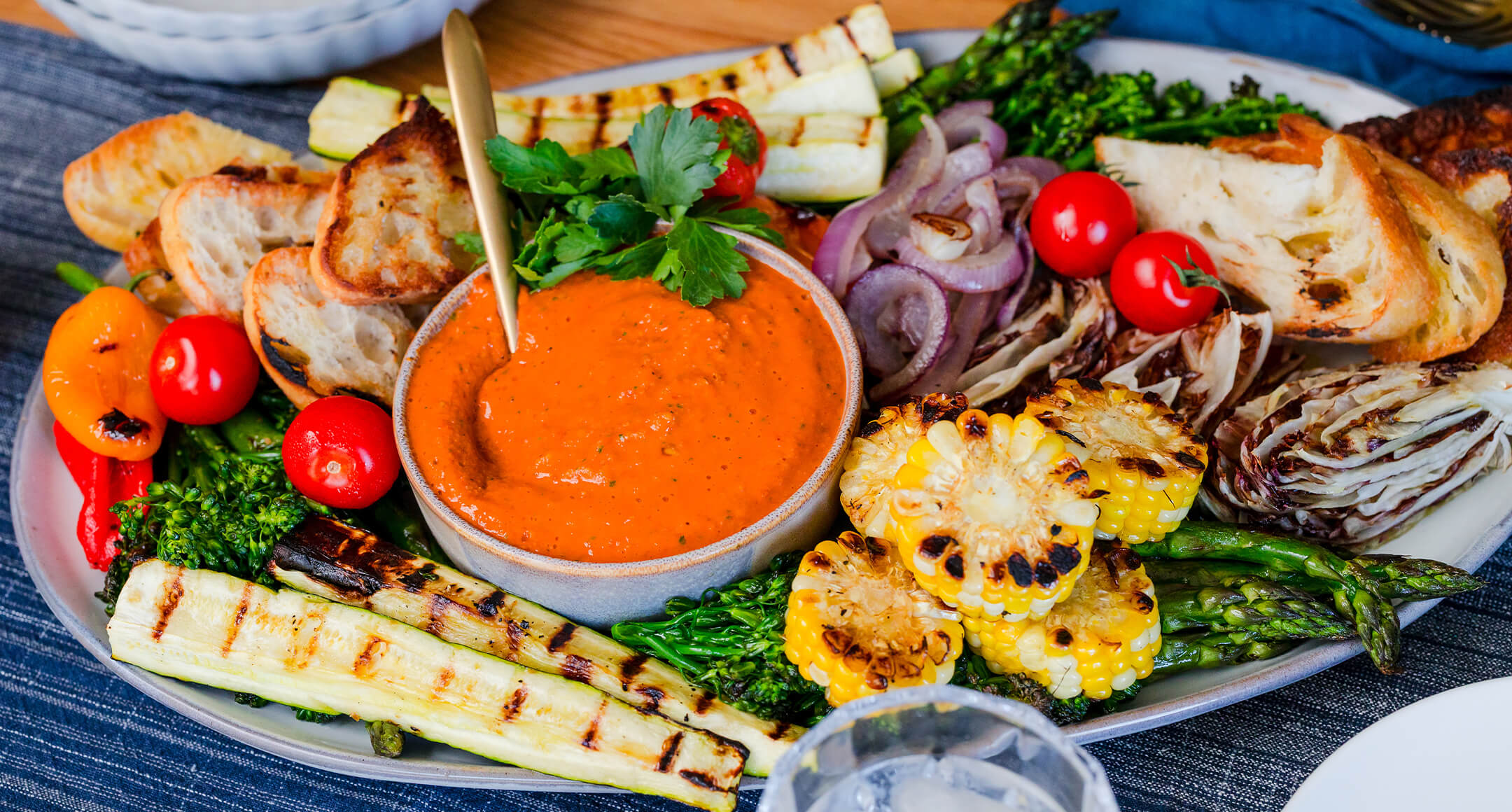 Romesco dip plated with grilled corn, bread, zucchini, onions, mini peppers and asparagus